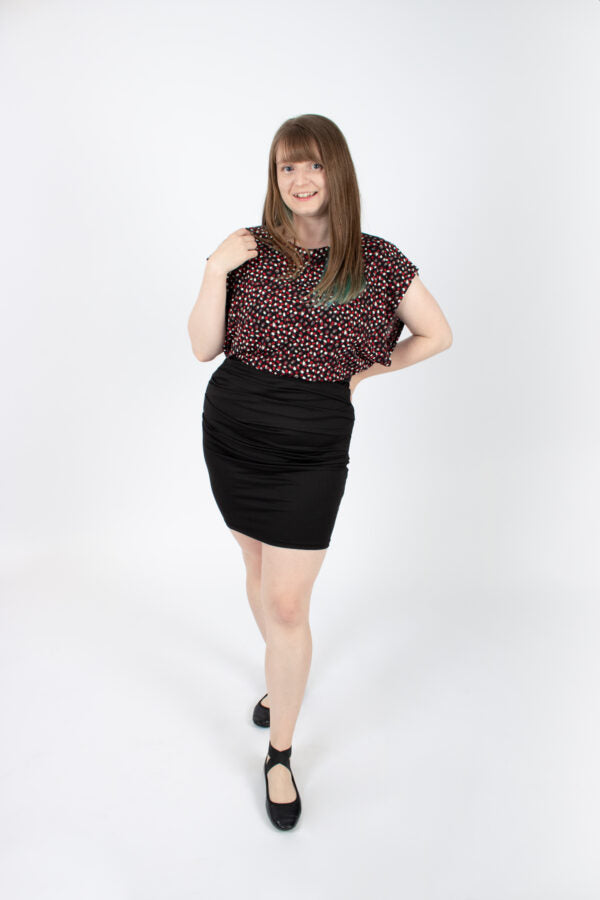 A woman wearing the Saki Top by Infime in Red brushstrokes with a black skirt, standing in front of a white background 