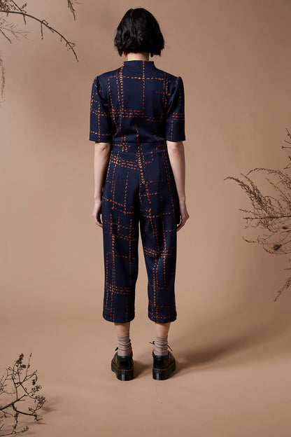 Back view of a woman wearing the Jonathan Jumpsuit by Melow in Indigo, standing in front of a beige background
