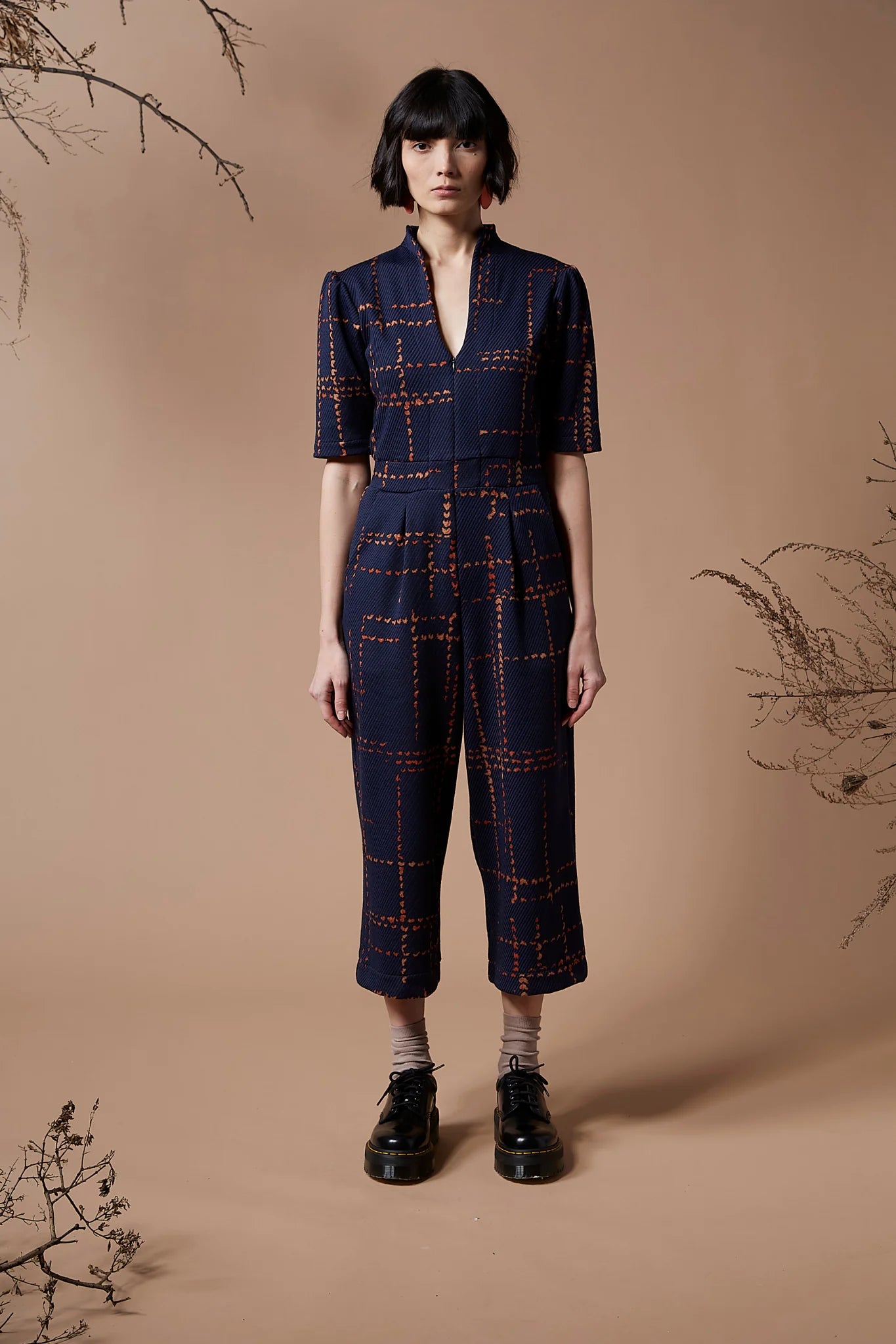 A woman wearing the Jonathan Jumpsuit by Melow in Indigo, standing in front of a beige background