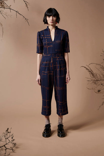 A woman wearing the Jonathan Jumpsuit by Melow in Indigo, standing in front of a beige background