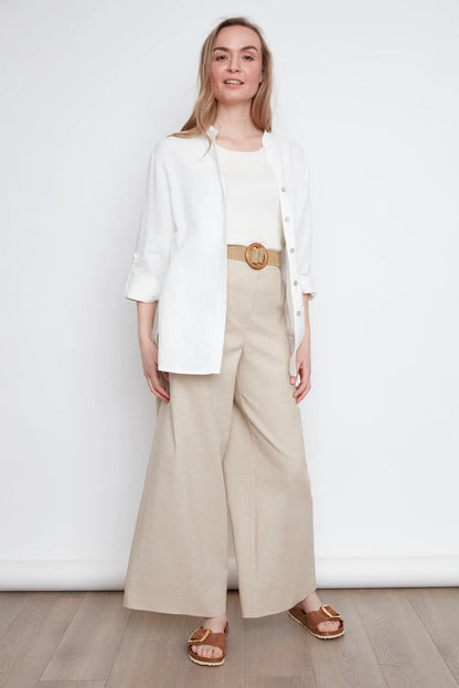 A woman wearing the jasmine Long Sleeve Shirt by Julei in Natural White, a classic dress shirt style with a mandarin collar, pleated pocket, and cuffed sleeves. She is wearing it with jeans and standing in front of white background. 
