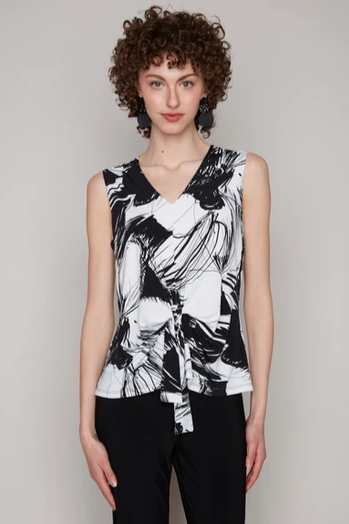 A woman wearing the Olivia Knit Top by Kollontai in an abstract Black and White pattern, a sleeveless top with a V-neck and a tie detail at the front.  She's wearing it with black pants and standing in front of a beige background.  