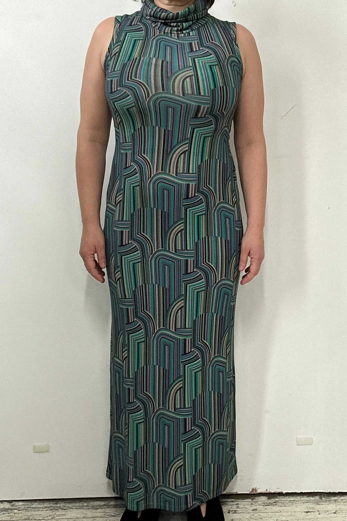 A woman wearing the Ysia Dress by Kollontai, a sleeveless turtleneck dress with a geometric pattern. She is standing in front of a white background. 