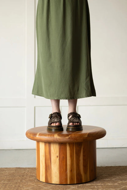 Waist down view of woman wearing the Simone Skirt by Lights of All in Cactus, a sleek calf-length skirt with a flared hem and an elastic waist. She is standing on top of wooden stool. 