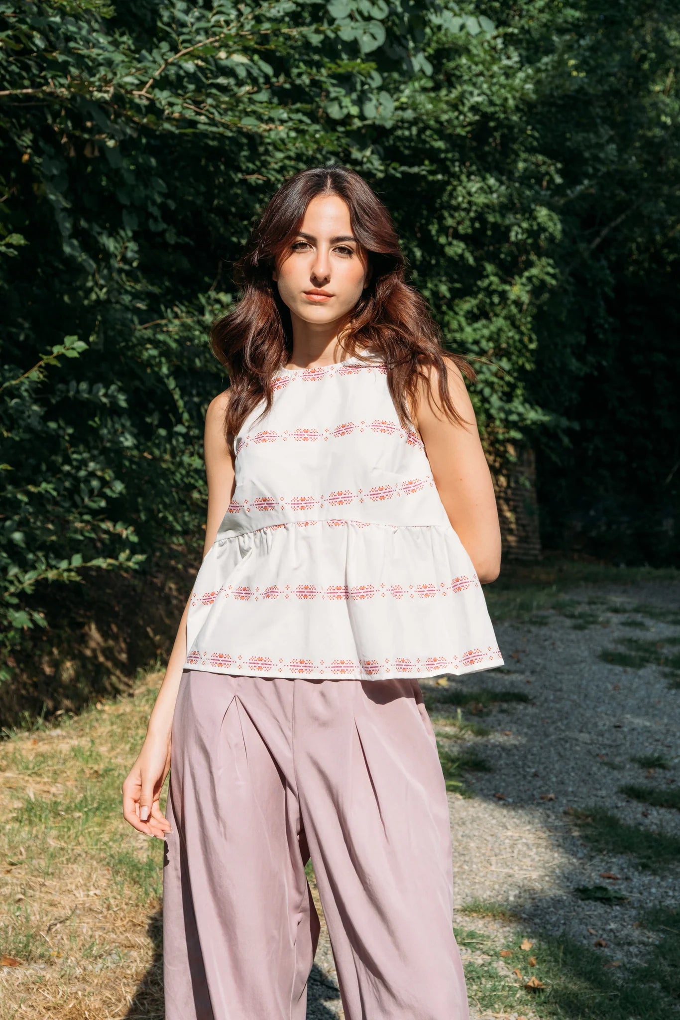 A woman wearing the Siena Pants by MAS in Raspberry, wide legged trousers with an elastic waist. She is wearing them with a white top and standing outdoors among trees.