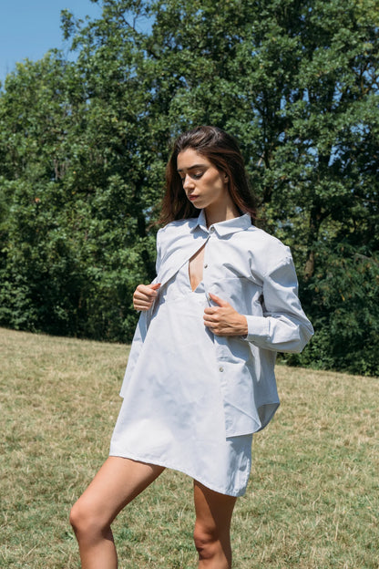 Woman wearing the Kyoto Blouse by MAS in Stripe, a classic collared button down with a cross-pleat at the back. She is wearing it open over a dress and standing outdoors. 