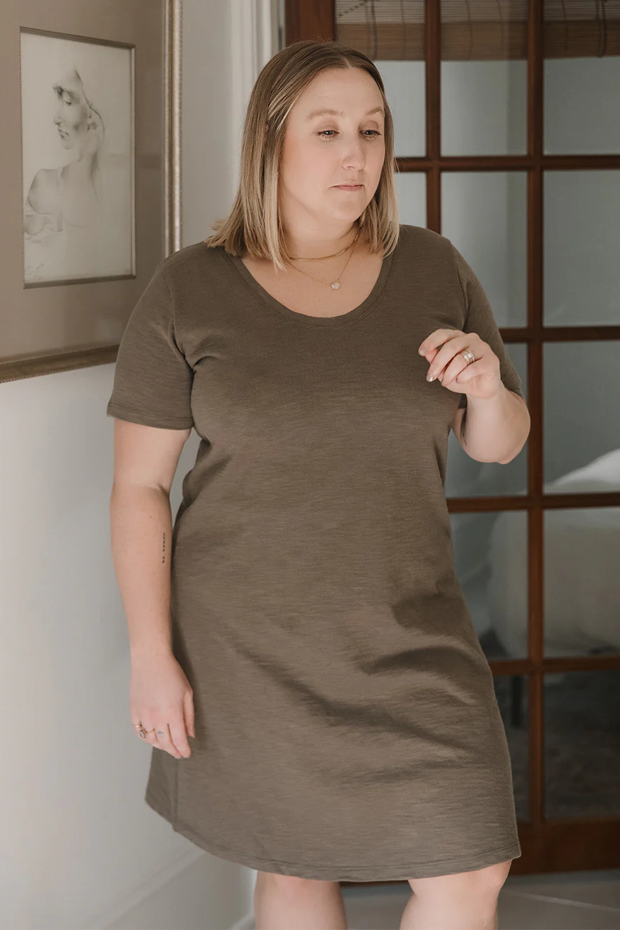 A woman wearing the Meadow Dress in Slub by Blondie Apparel in Clay, standing in front of a doorway