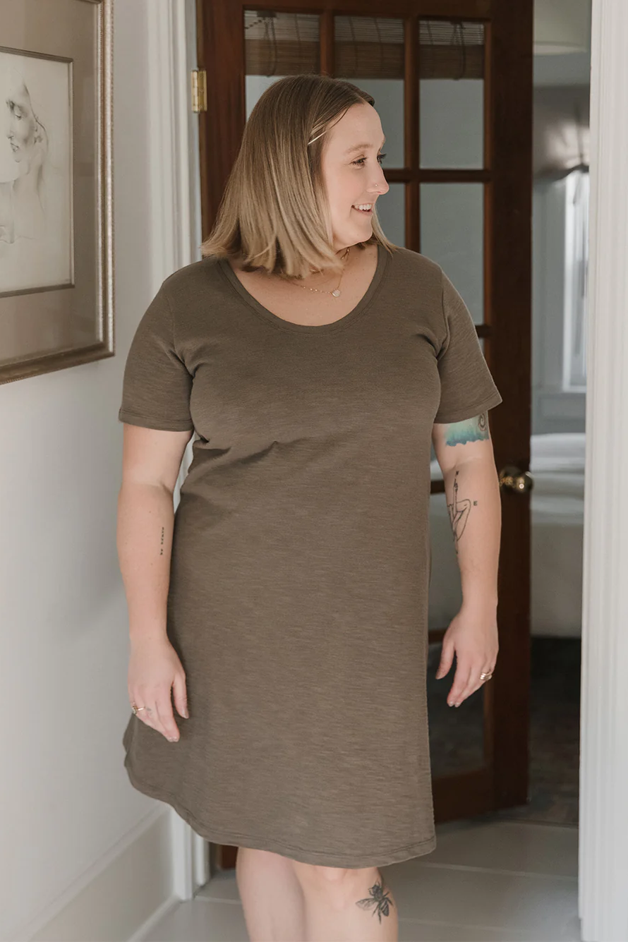 A woman wearing the Meadow Dress in Slub by Blondie Apparel in Clay, standing in front of a doorway