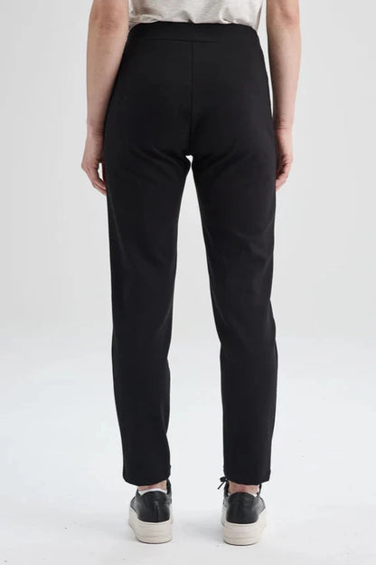 Back waist-down view of the Sherbrooke Pants by Message Factory in Black, pull-on semi-fitted pants with side pockets made from Lenzing Ecovero viscose. She is standing in front of a white background. 