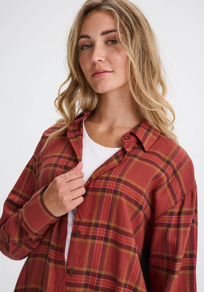Waist up view of a woman wearing the Donnacona Shirt Dress by Message Factory in Rust Check, a knee-length dress with a button front and collar. She is wearing it open over a white t-shirt and standing in front of a white background. 