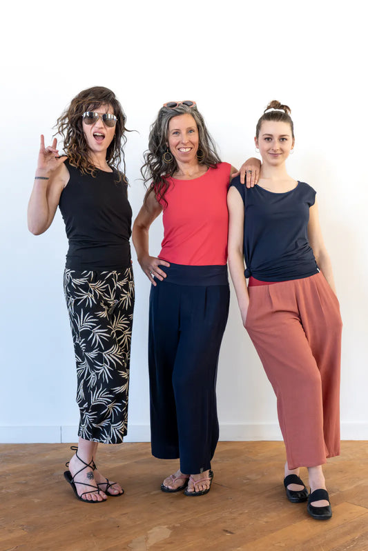 Three women wearing the Verano Pants by Marie C in various colours, they are wearing them with Sol tops and standing in front of a white wall. 