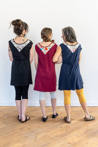 Back view three women wearing the Mariposa Dress by Marie C, a short sleeved short dress that's reversible back to front with printed yoke on one side, and an attached tie belt. The one in the centre is wearing it in Raspberry. 