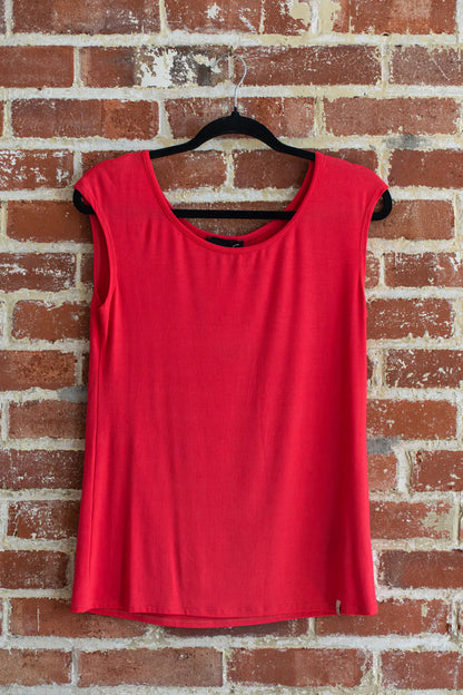 The Sol Top from Marie C in Coral, a reversible cap sleeve tee, is shown hanging vertically in front of a brick wall.