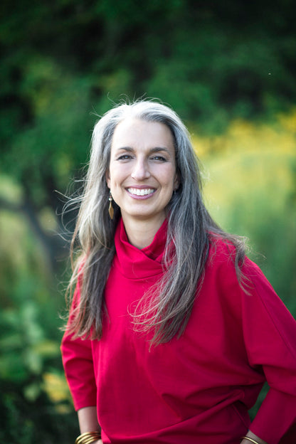 A woman wearing the BeAAA Sweater by Marie C in Red, standing in a field 