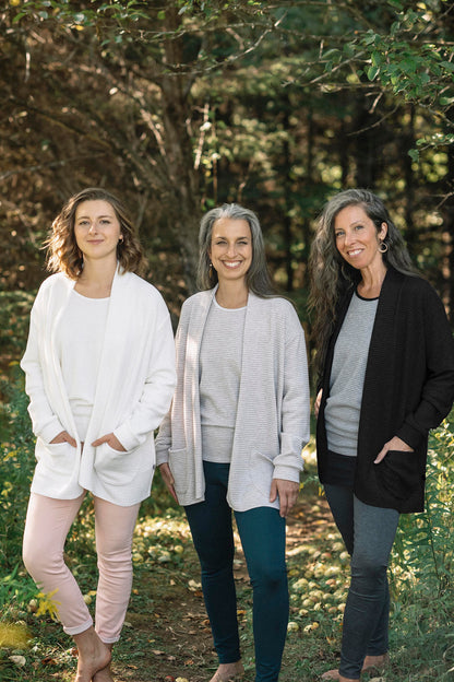 Two women wearing the Perla Top by Marie C,  one in Ivory and one in Black, with a wide round neck, 3/4 batwing sleeves, and fitted waist in ribbed knit fabric. They each wearing the Margo Cardigan over top and are standing outside. 