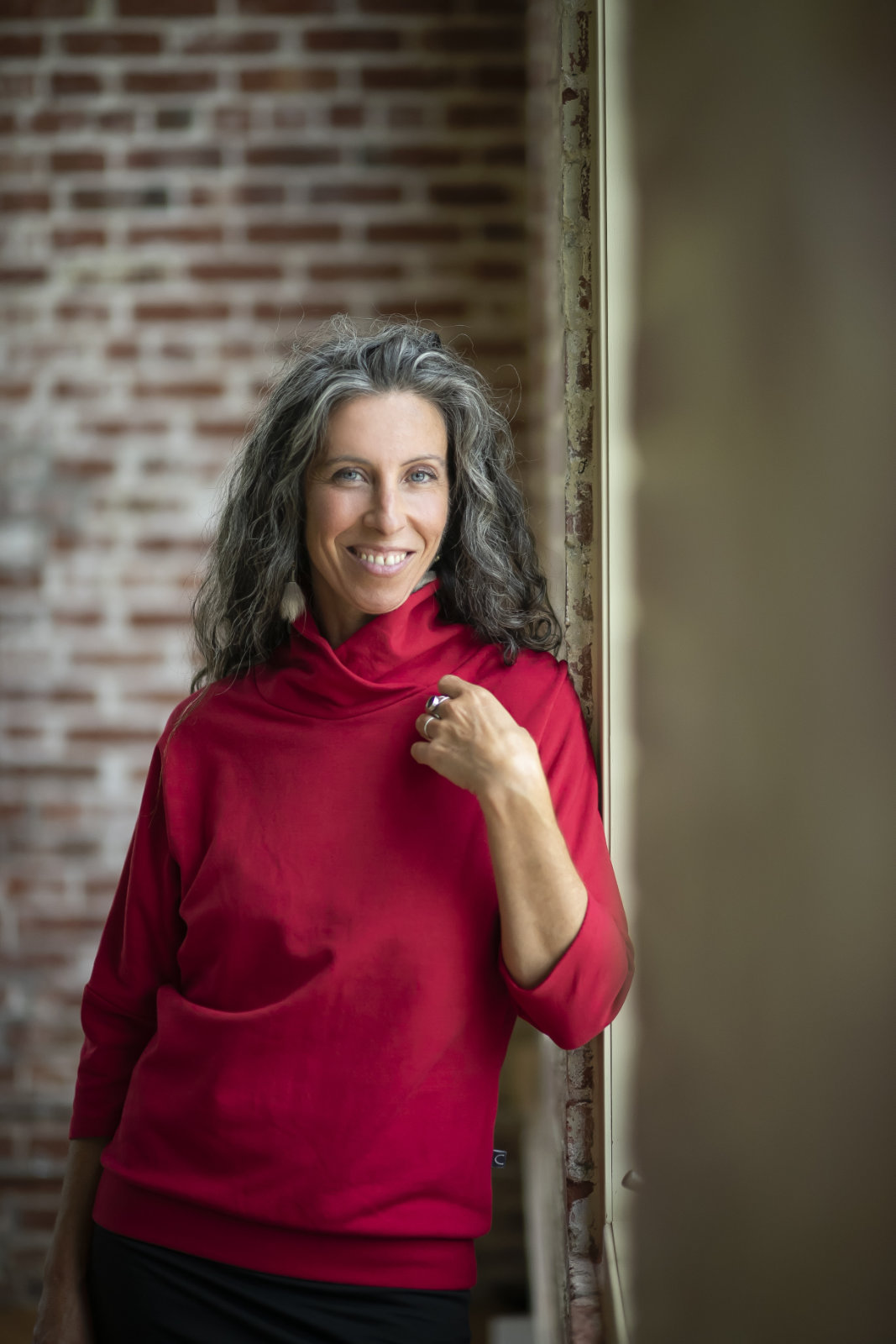 A woman wearing the Beaaa Top by Marie C in Red, standing in front of a brick wall 