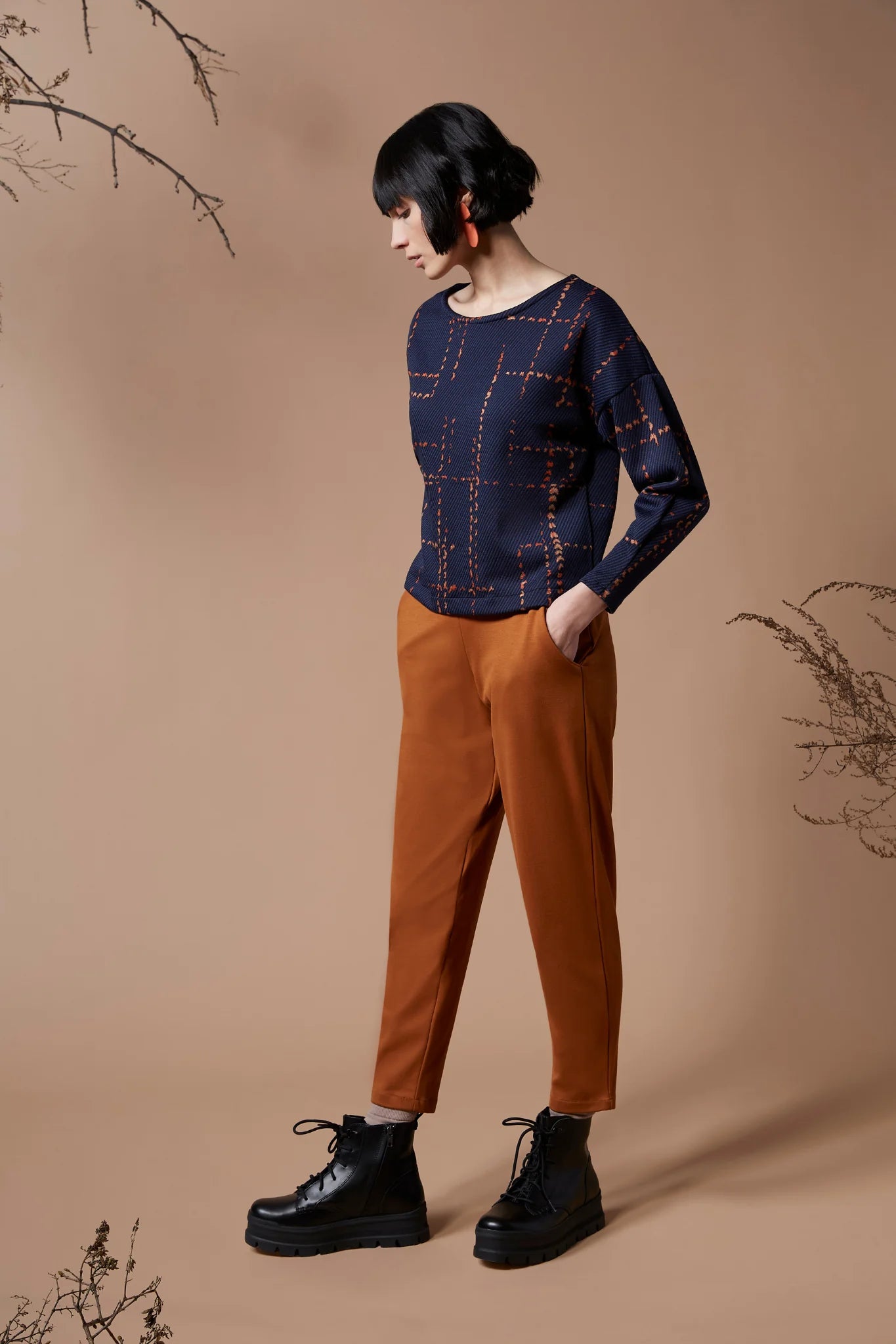 A woman wearing the Jackson Top by Melow in indigo with orange pants, standing in front of a peach background 