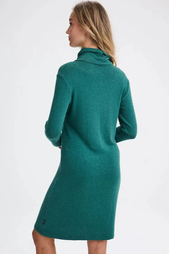 Back view of a woman wearing the Betula Dress by Message Factory in Evergreen, a knit turtleneck dress with long sleeves and a knee-length hem. She is standing in front of a beige background. 
