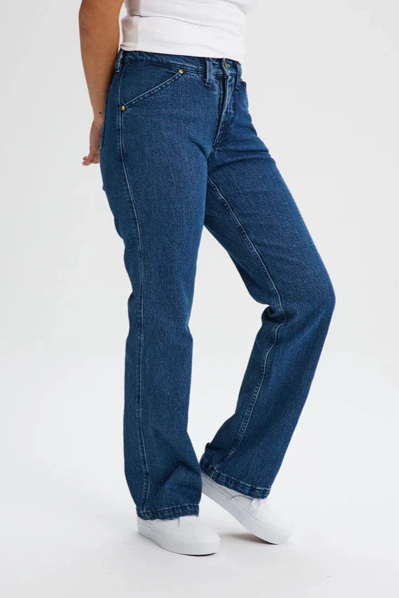 Waist down view of a woman wearing the Marianne Straight Leg Denim Pants by Message Factory, featuring a straight leg, a 31 inch inseam, and organic cotton fabric, with a white tank. She is standing in front of a white background. 