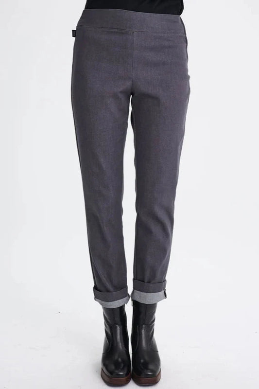 Waist-down view of a woman wearing the Potton Pants by Message Factory in Gray Denim,  slim cut pants in stretchy denim with a wide waistband and a side zipper, made from recycled cotton and polyester. She's standing in front of a white background. 