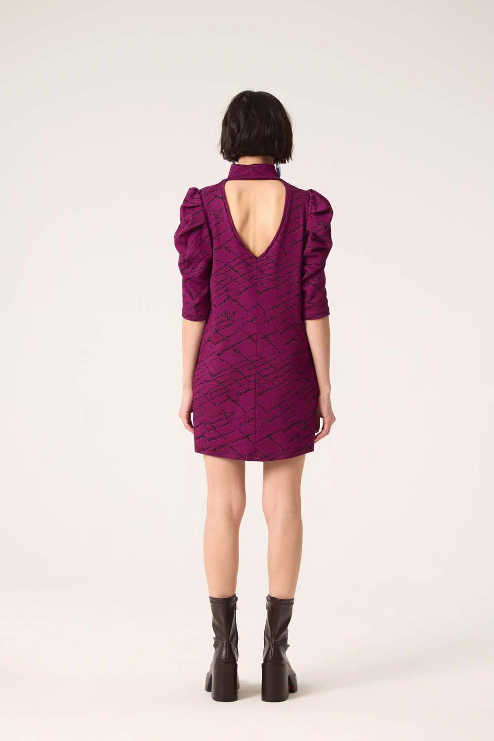 Back view of a woman wearing the Nostalgia Dress by Cokluch in Magenta, standing in front of a white  background.