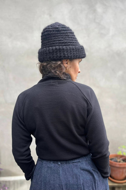 Back view of a woman wearing the Oris Raglan Turtleneck by Kazak in Black waffle. She is wearing it with jeans and standing outside. 