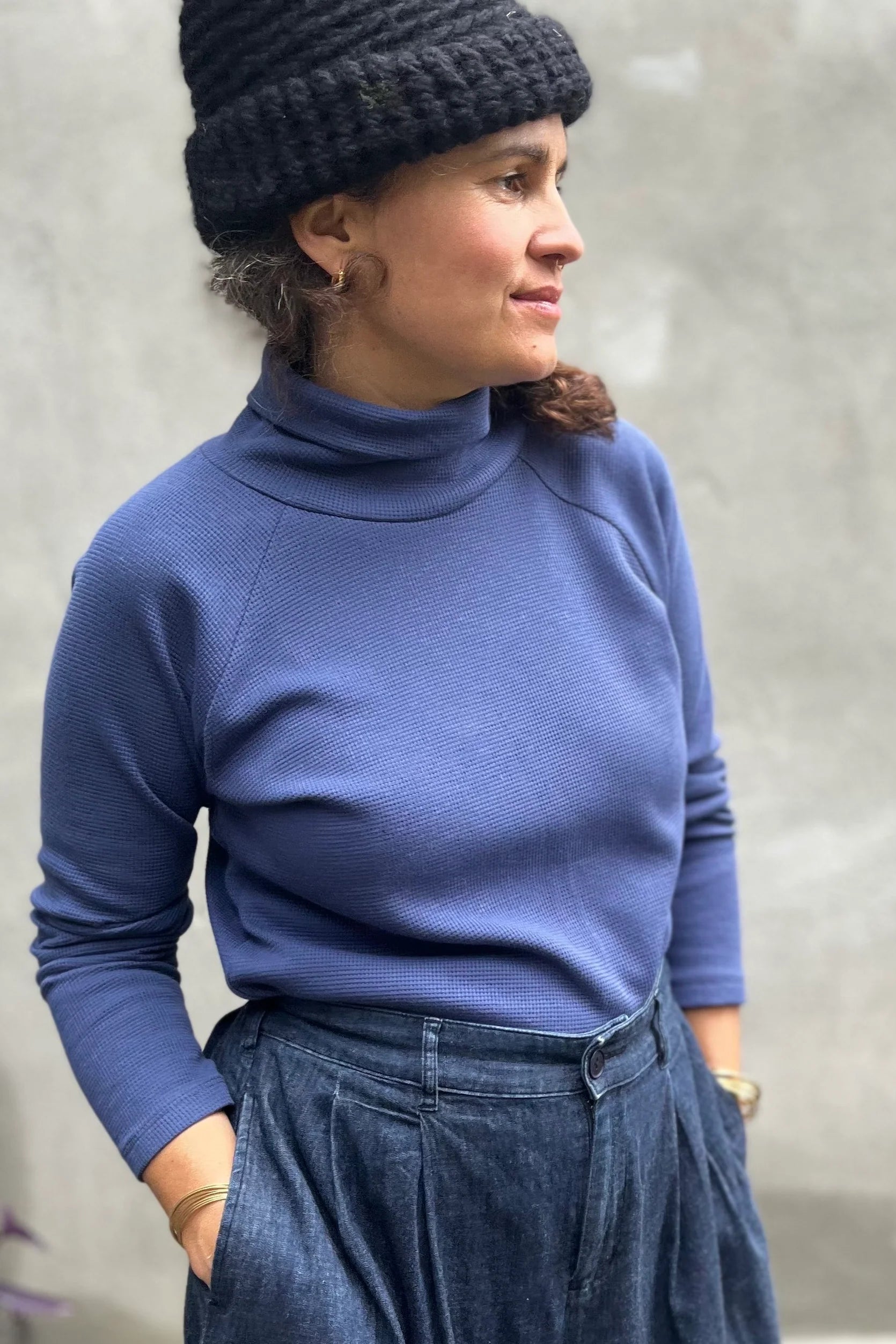 A woman wearing the Oris Raglan Turtleneck by Kazak in Indigo waffle. She is wearing it with jeans and standing outside. 