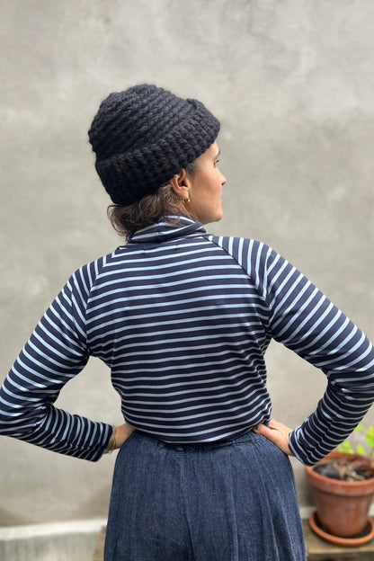 A woman wearing the Oris Raglan Turtleneck by Kazak in Blue Stripe. She is wearing it with jeans and standing outside. 