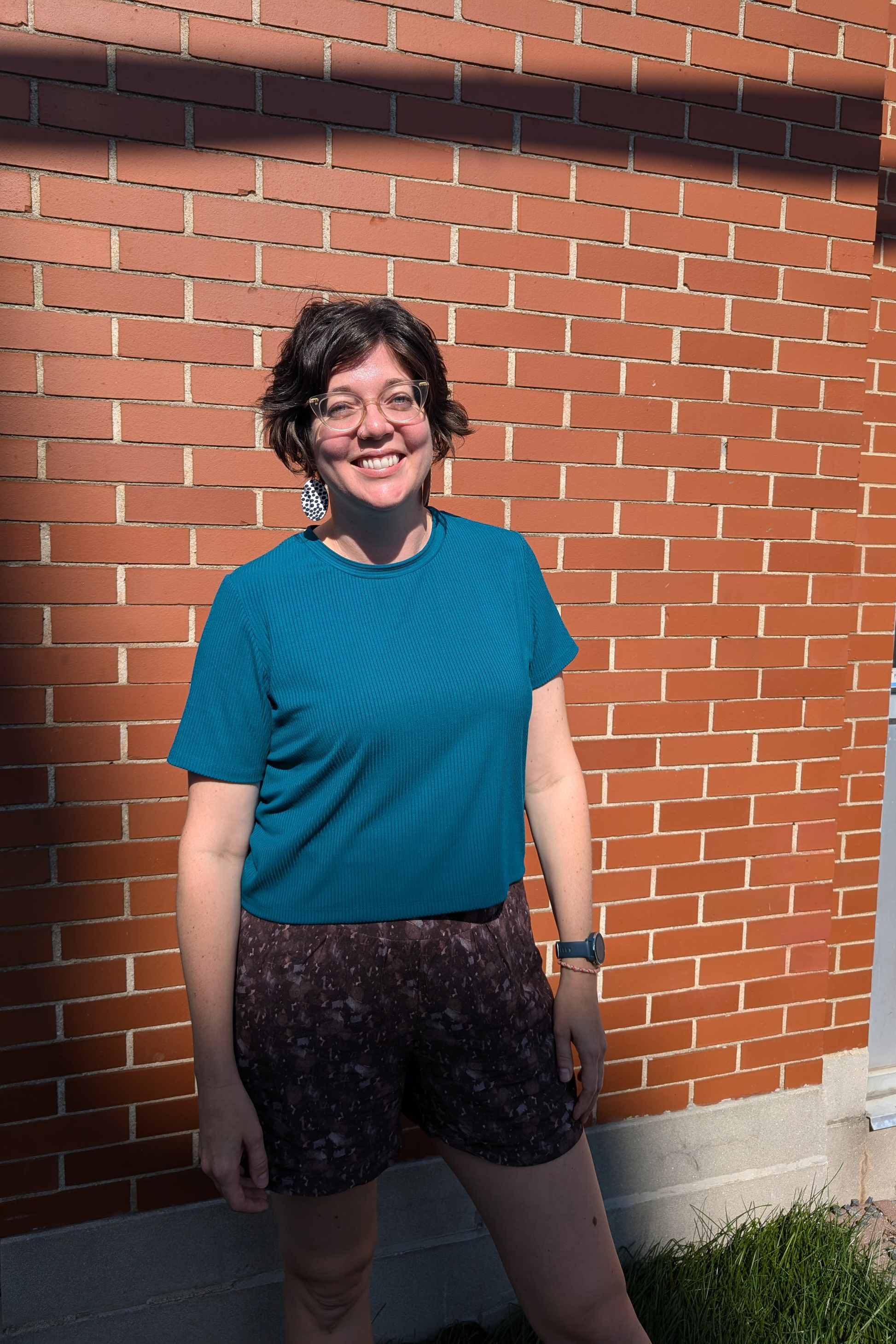 Val wearing the Flock Exclusive Porto T-shirt by MAS in Teal, standing in front of the brick wall outside of Flock