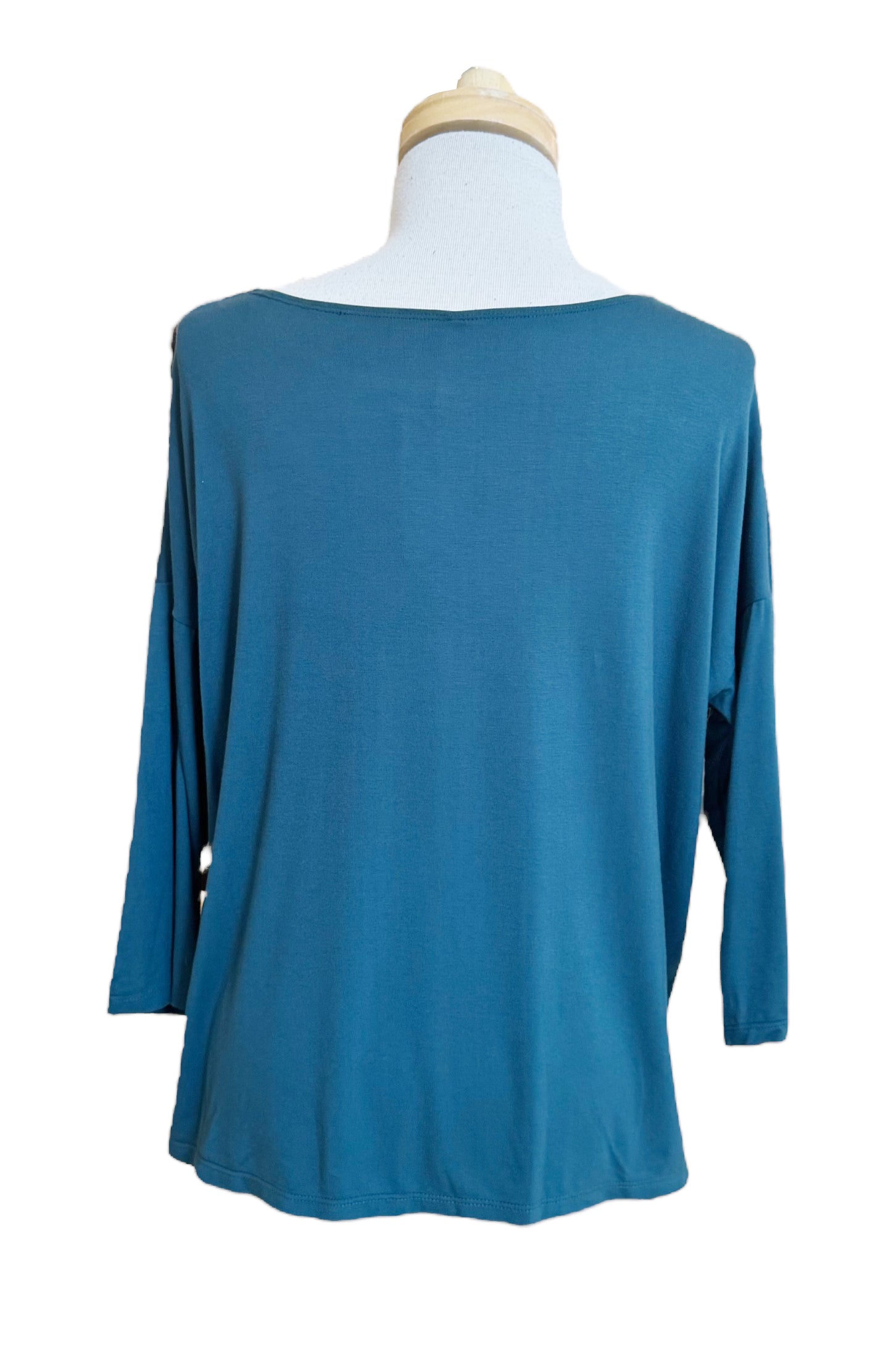 A back view of The Emmy Top by Moovment in Teal, with a boat neck, 3/4 sleeves, and side slits, is shown on a mannequin in front of a white background.
