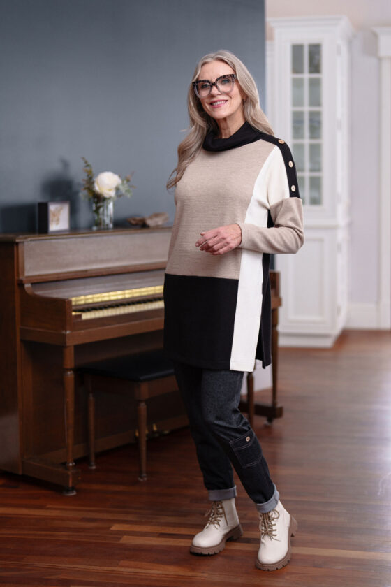 A woman wearing the Goya Pants by Rien ne se Perd in Grey, faux-denim leggings with an elastic waistband and decorative side pockets. She's wearing them with the Rembrandt Tunic and standing in front of a piano. 