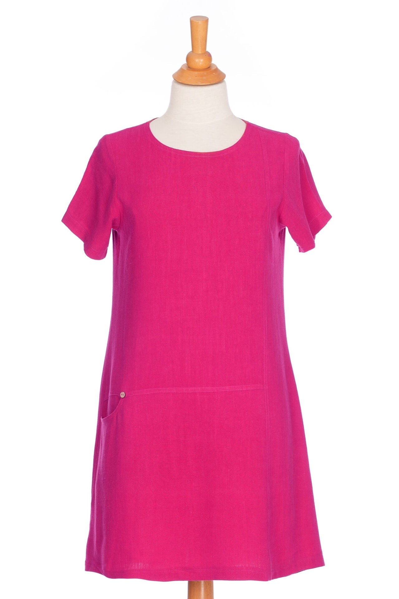 The Merengue Tunic by Rien ne se Perd in Raspberry, a loose-fitting linen and viscose tunic with a round neck, short sleeves, asymmetrical cut, and patch pocket, is shown on a mannequin in front of a white background. 