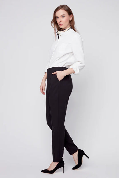 A woman wearing the Sarah Cigarette Pant by Julei in Black, featuring four way stretch fabric, pin tucks for shape, and a pull-on waist. She is wearing them with a white shirt and standing in front of a white background. 