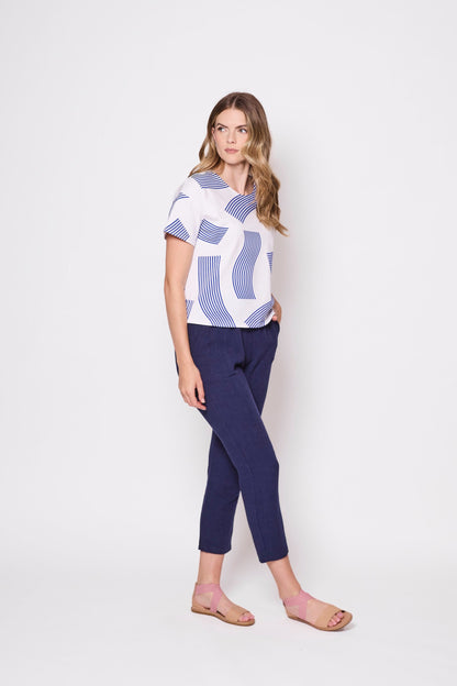 3/4 shot of a woman wearing the Waverly T-Shirt by Tangente in Blue, a slightly boxy tee with a wavy striped print on a white background. She is wearing it with blue pants and standing in front of a white background. 