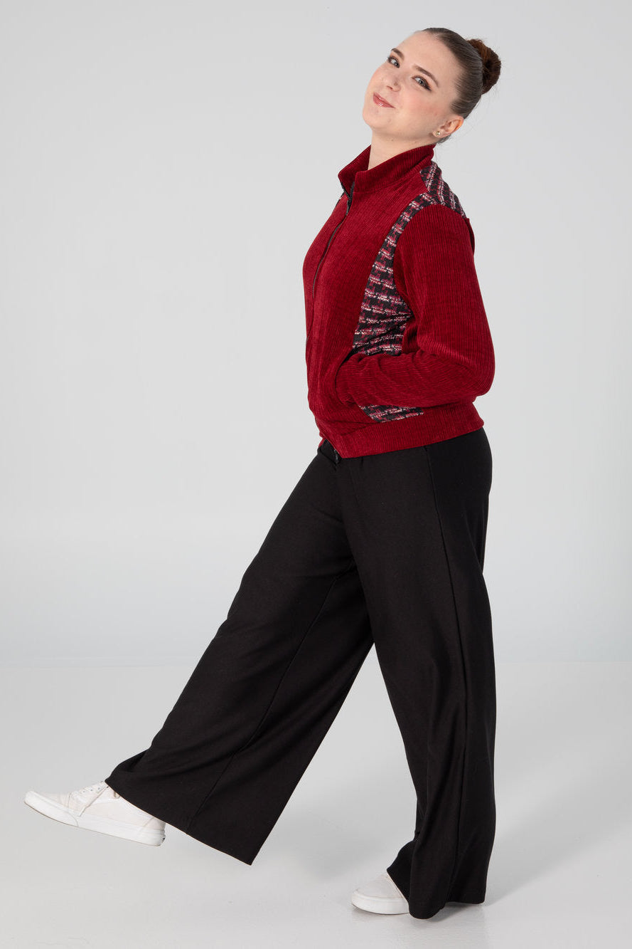 Side view of a woman wearing the Enfield Jacket by Slak, a bomber style jacket in textured burgundy fabric with plaid panels at the sides and across the upper back. She is wearing it with black pants and standing in front of a white background. 