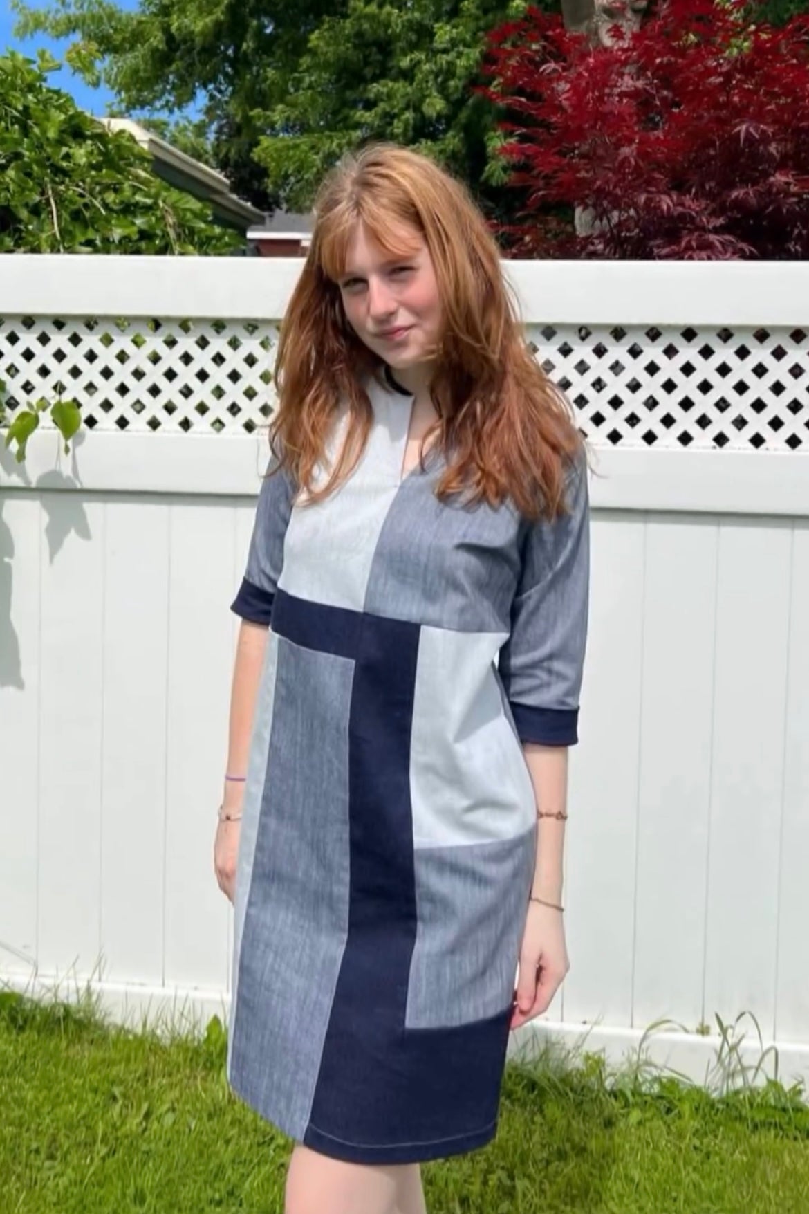 A woman wearing the Serena Dress by Solomia in Navy/Grey/White colourblocking, standing in front of a white fence