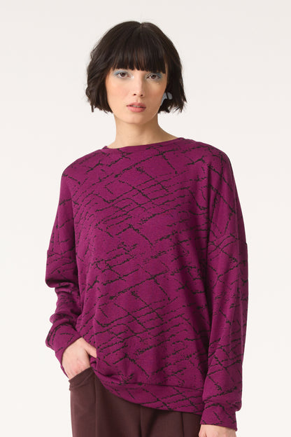 Semi close-up of a woman wearing the Space Sweater by Cokluch in Magenta, standing in front of a white background 