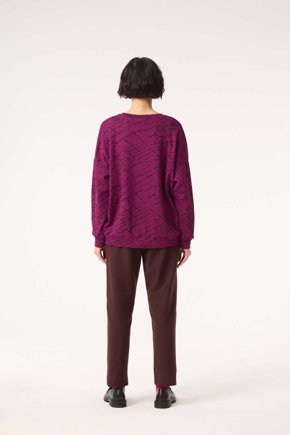 Back view of a woman wearing the Space Sweater by Cokluch in Magenta, with the Belief Pants in Shiraz, standing in front of a white background 