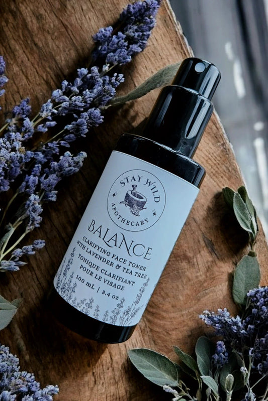 Bottle of 'Balance' face mist by Stay Wild Apothecary shown with lavender flowers on a wooden surfac