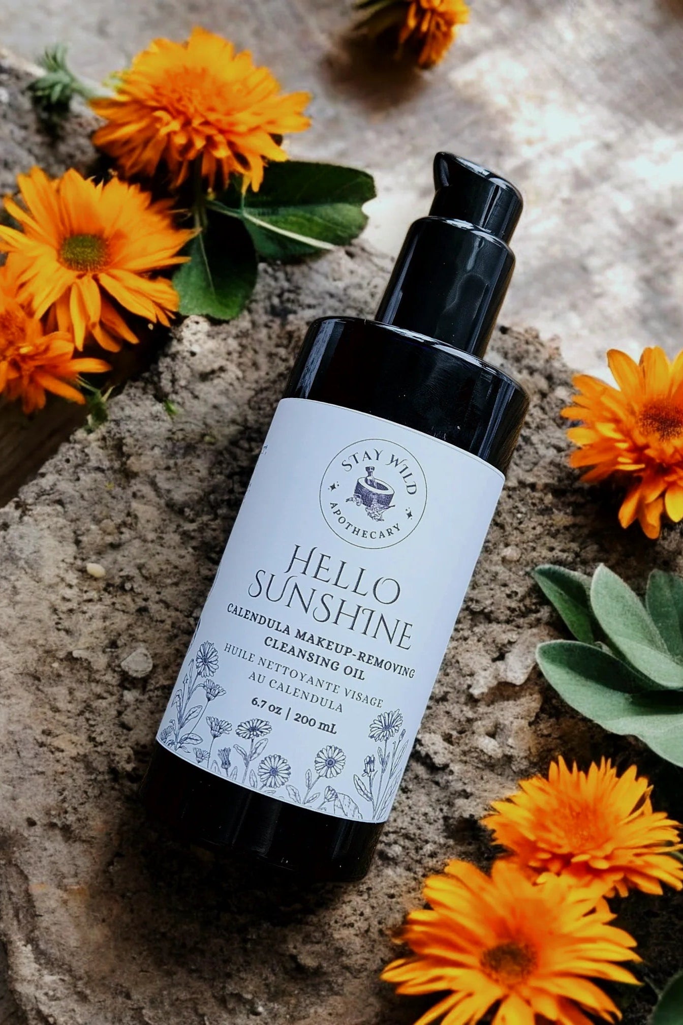 Bottle of 'Hello Sunshine' cleansing oil  by Stay Wild Apothecary with calendula flowers on a stone surface
