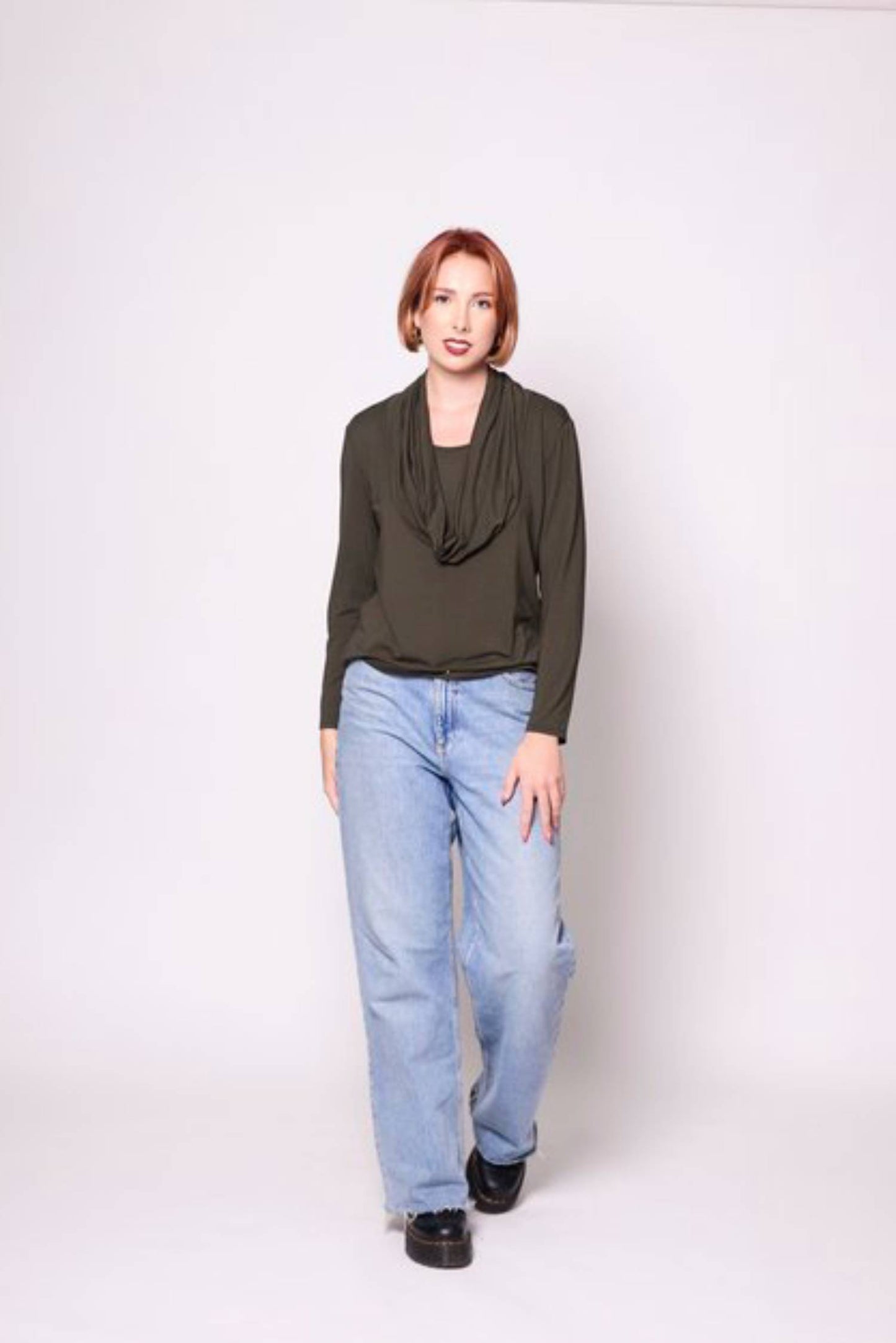 A woman wearing the Lauren Top by Tangente in Spruce with jeans, standing in front of a white background 