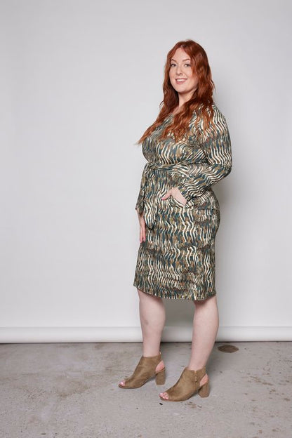 Side view of a woman wearing the Gwen Dress by Tangente in Green print, standing in front of a white background 