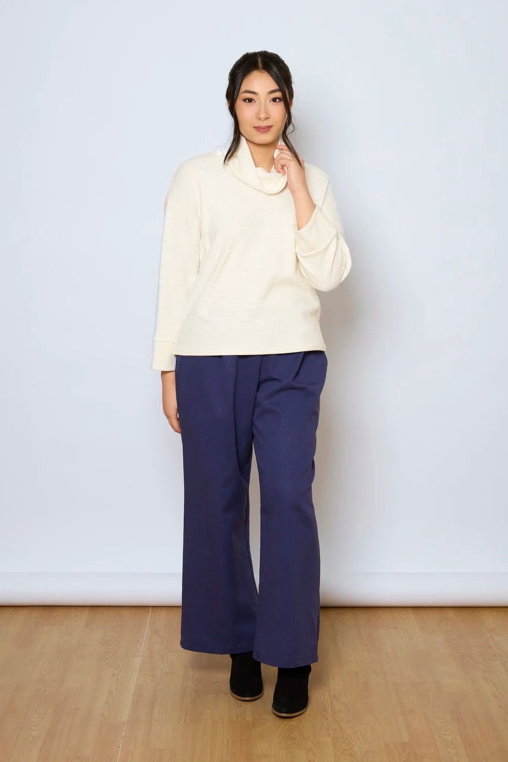 A woman wearing the Jill Pants by Tangente in Denim, wide-legged ankle length pants with large pockets. She is wearing them with a white sweater against a white background.
