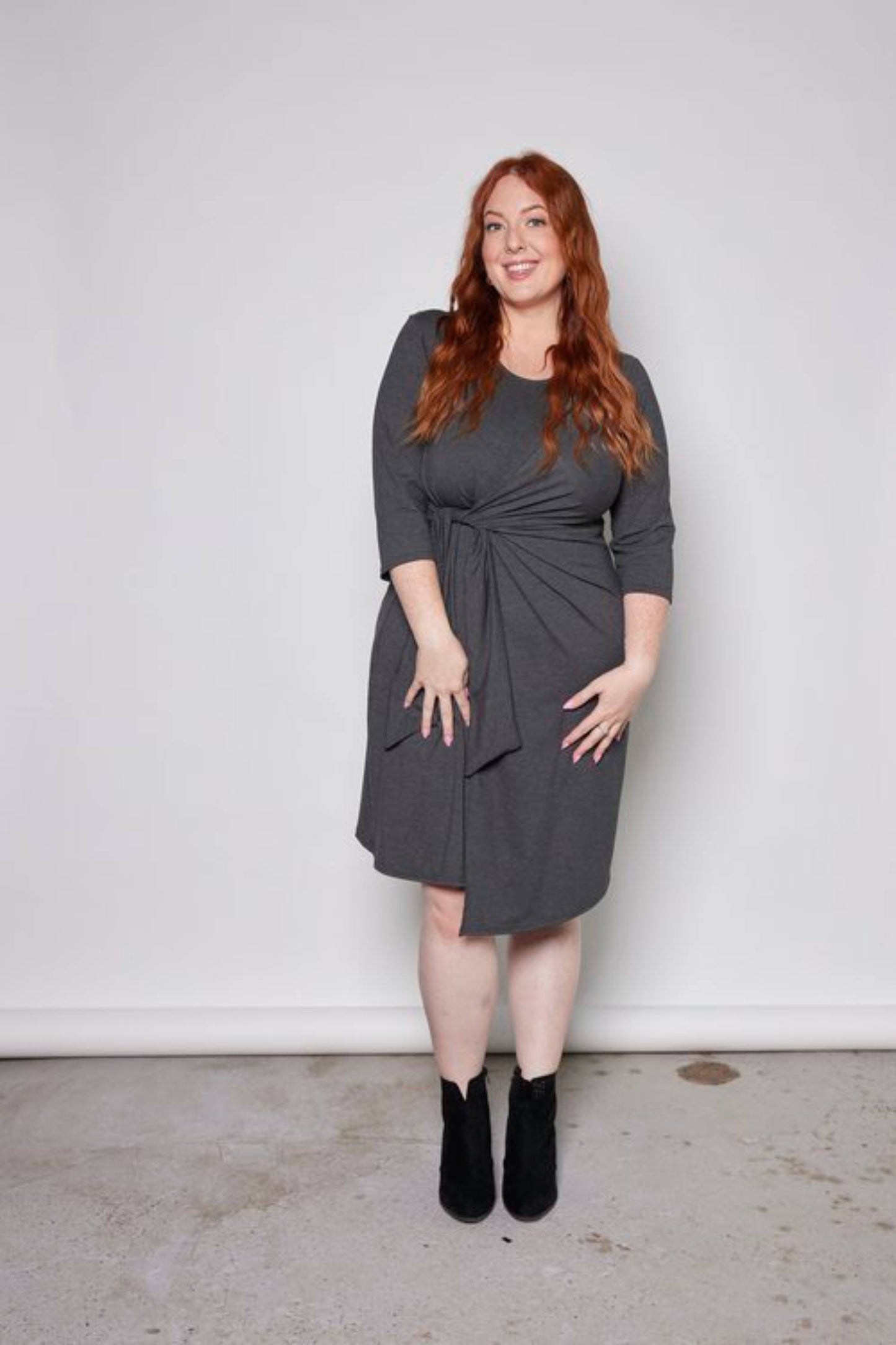 A woman wearing the Mariela Dress by Tangente in Charcoal, standing in front of a white background 