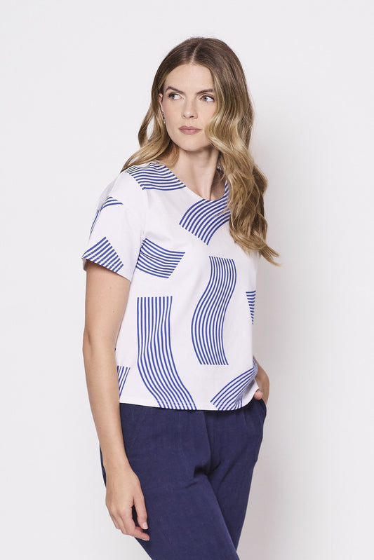 3/4 shot of a woman wearing the Waverly T-Shirt by Tangente in Blue, a slightly boxy tee with a wavy striped print on a white background. She is wearing it with blue pants and standing in front of a white background. 