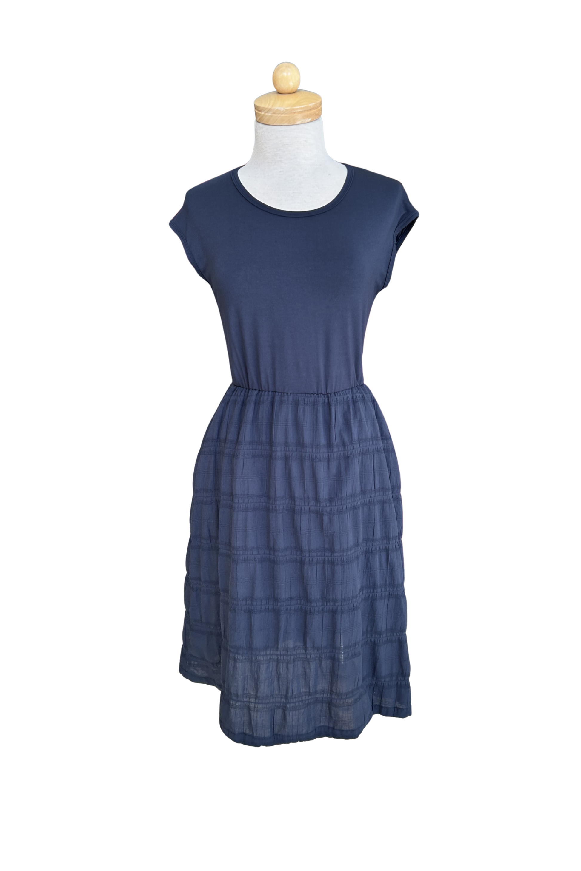 The Mona Dress by Tangente in Navy, a below the knee length dress featuring a bamboo rayon bodice and seersucker skirt, with short sleeves and a round neck, is shown on a mannequin against a white background. 