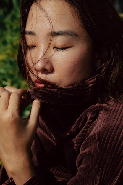 A woman wearing the Amsterdam Sweater by MAS in Cacao, an oversized ribbed velvet sweater with a chimney neckline and long batwing sleeves. 
