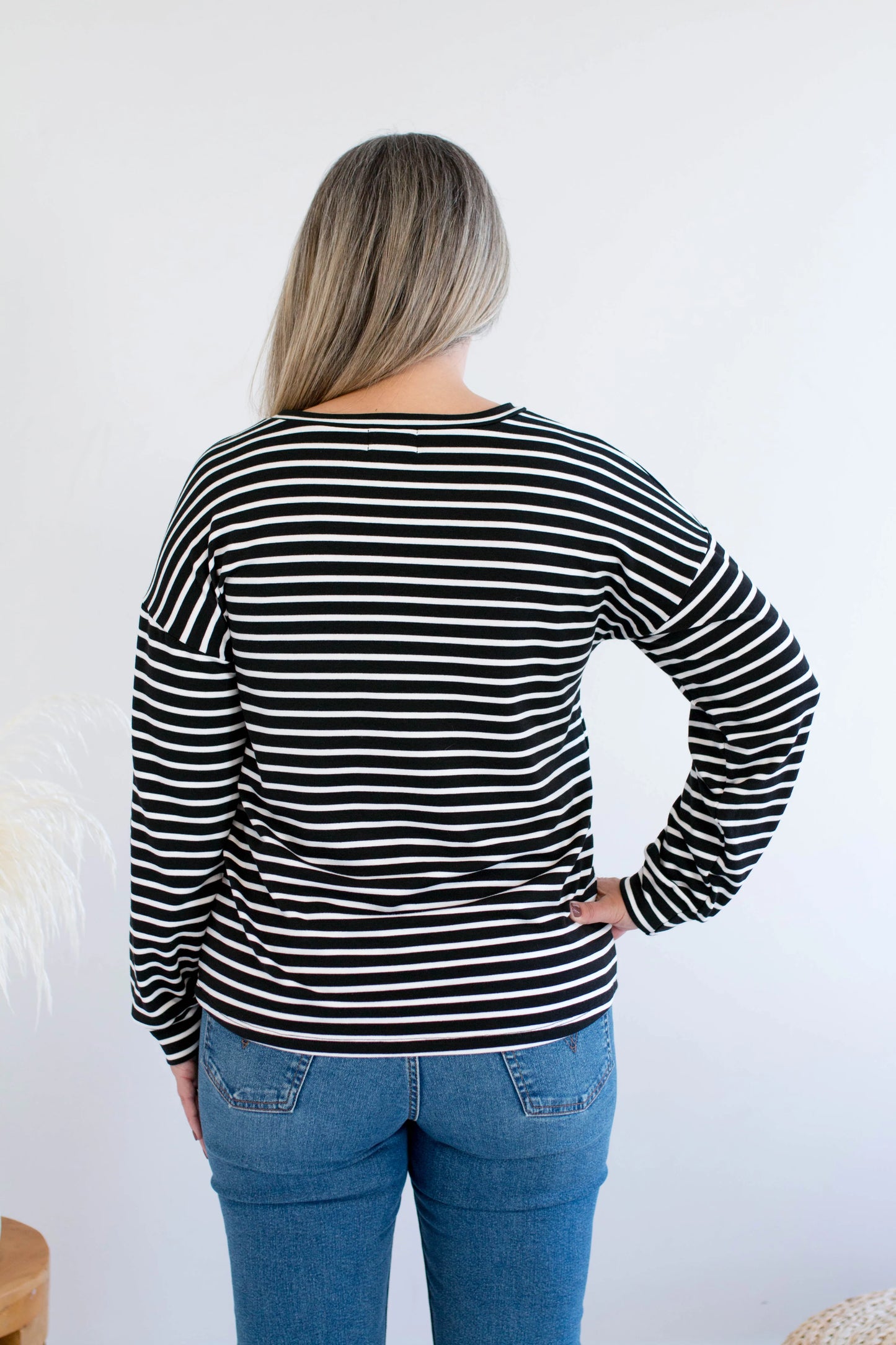Back view of a woman wearing the Munro Bamboo Crewneck sweater by Ang Hill in black and white stripes. She is wearing it with jeans against a white background.