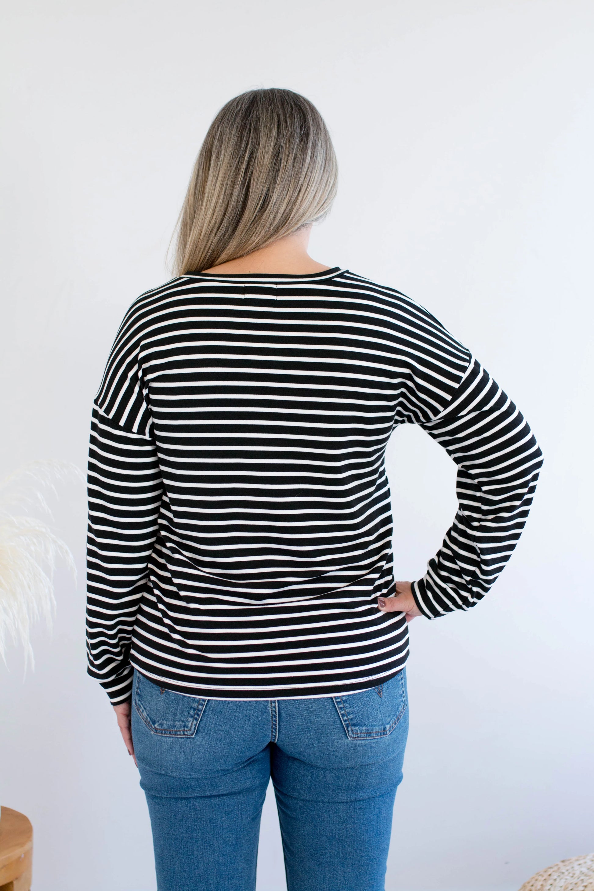 Back view of a woman wearing the Munro Bamboo Crewneck sweater by Ang Hill in black and white stripes. She is wearing it with jeans against a white background.