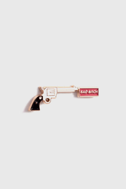 The Bad Bitch Pin by Badaboöm Studio, featuring a gold gun with a red banner that reads "Bad Bitch", is shown against a white background. 